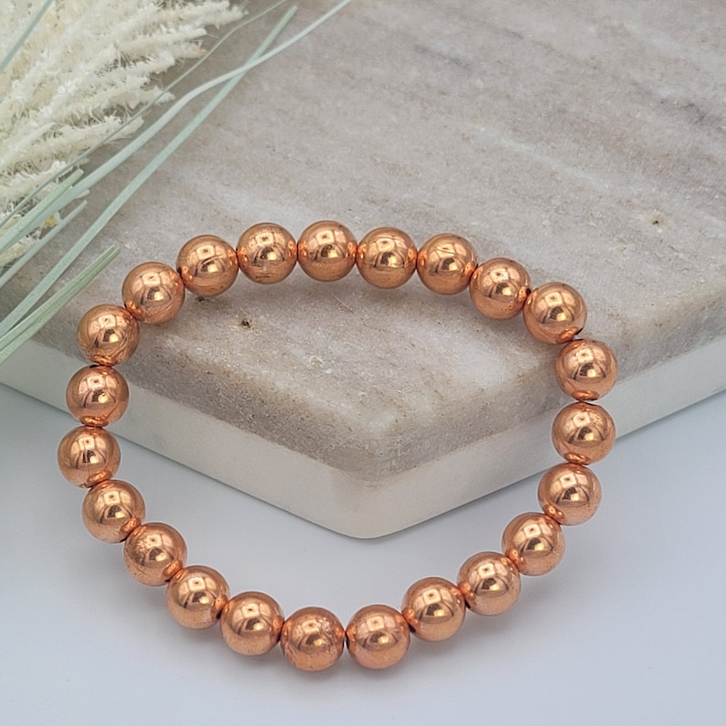 May include: A copper beaded bracelet with a natural, earthy look. The bracelet is made of round, copper beads that are strung together on a stretchy cord.