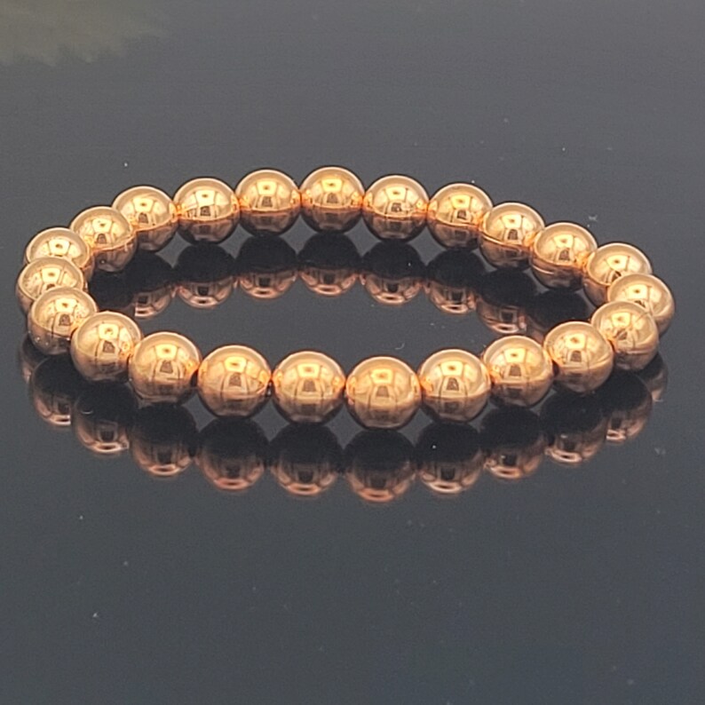 May include: A rose gold beaded bracelet with a shiny finish. The bracelet is made of round beads and is approximately 7 inches in length.