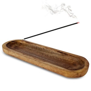 May include: A wooden incense holder with a natural finish. The holder is a long, oval shape with a curved design. A lit incense stick is placed in the holder, with smoke rising above it. The background is white.