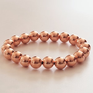 May include: A copper beaded bracelet with a shiny finish. The bracelet is made of round beads and is approximately 7 inches in length.