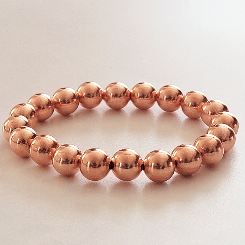 May include: A copper beaded bracelet with a shiny finish. The bracelet is made of round beads and is approximately 7 inches in length.