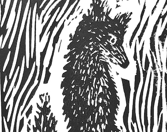 May include: Black and white linocut print of a fox sitting in a forest. The fox is depicted with detailed fur and a pointed snout, surrounded by stylized trees and foliage. The artwork has a rustic, handmade aesthetic.