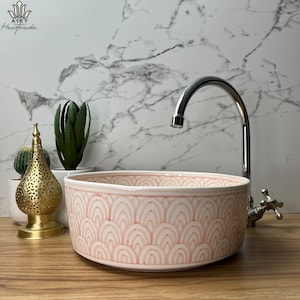 May include: A pink ceramic bathroom sink with a white geometric pattern. The sink is round and has a chrome faucet.