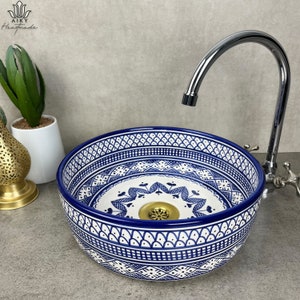 May include: A white ceramic sink with a blue and white geometric pattern. The sink is round and has a drain in the center. A chrome faucet is visible in the background.
