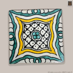 Peut inclure: Carreau de céramique carré avec un motif peint à la main. Le carreau présente un carré jaune central avec un motif de losanges noirs, entouré d'une bordure blanche avec des accents turquoise et jaunes. Un motif floral turquoise est au centre.