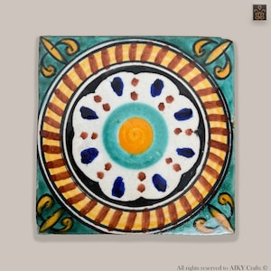 Peut inclure: Un carreau de céramique carré avec un motif géométrique coloré. Le centre du carreau présente une fleur blanche avec des accents bleus et bruns, entourée d'un cercle turquoise avec un centre jaune. La bague extérieure du carreau est un motif rayé noir et jaune.