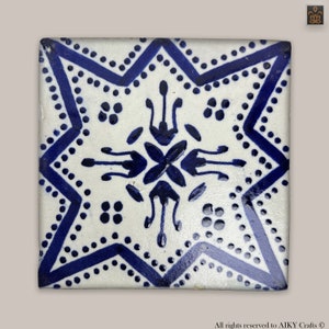 Peut inclure: Un carreau de céramique blanc avec un motif en étoile bleu et blanc. Le carreau a une étoile bleue au centre avec une petite fleur bleue au centre de l'étoile. L'étoile est entourée d'un anneau de points bleus et d'un anneau de lignes bleues.