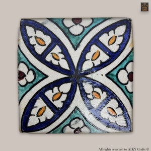 Peut inclure: Un carreau de céramique carré avec un motif géométrique bleu, blanc et vert. Le carreau présente un motif répétitif de fleurs et de feuilles stylisées.