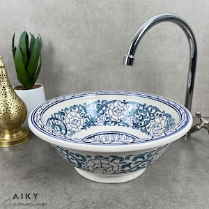Könnte beinhalten: Weiße Keramikspüle mit einem blauen und grünen floralen Muster. Die Spüle ist rund und hat einen breiten Rand. Ein verchromter Wasserhahn ist im Hintergrund sichtbar.