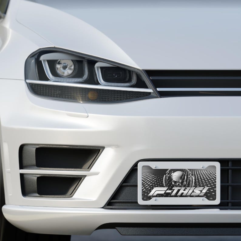 May include: Close-up of a white car's front end, showcasing a license plate with a skull design and the text "F-THIS!". The car's headlights and bumper are also visible.