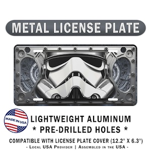 May include: A rectangular metal license plate featuring a graphic of a white stormtrooper helmet centered against a dark, industrial background. The plate has a metallic border with visible rivets and four pre-drilled mounting holes. Dimensions are 12.2 inches by 6.3 inches.