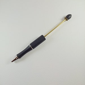 Könnte beinhalten: Ein schwarzer Stift mit einer silbernen Spitze und einer goldenen Metallerweiterung mit einer schwarzen Gummspitze.