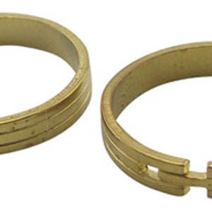 May include: Two gold-colored adjustable rings. Each ring has a simple design with two parallel lines etched around the band. The rings have a clasp mechanism for adjusting the size. The rings are made of a shiny, metallic material.