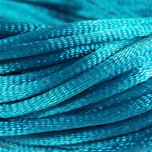 Op de afbeelding: Close-up van een spoel tealblauwe draad. De draad is strak gewikkeld en heeft een gladde, zijdeachtige textuur.