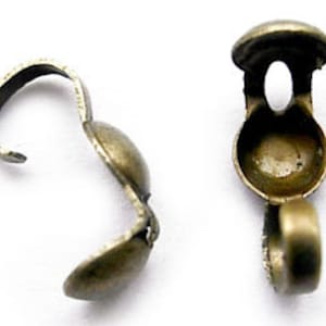 May include: Two antique gold-toned metal clasps for jewelry making. Each clasp has a round, slightly domed top with a small opening. The clasps are designed to be used with a cord or chain.
