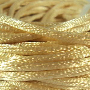 Può includere: Primo piano di un rocchetto di filo da ricamo color crema. Il filo è morbido e setoso, ideale per una varietà di progetti di artigianato.