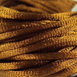 May include: A close-up of a spool of brown satin cord. The cord is tightly wound and has a smooth, shiny finish.