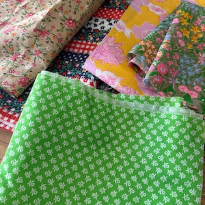 May include: A collection of folded fabric pieces featuring various patterns including a bright green cloth with small white flowers, a yellow fabric with pink floral designs, a beige cloth with red and green flowers, and a red and white checkered textile.