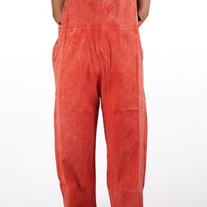 May include: Red denim overalls with a small embroidered design on the front pocket. The overalls have adjustable straps and a relaxed fit.
