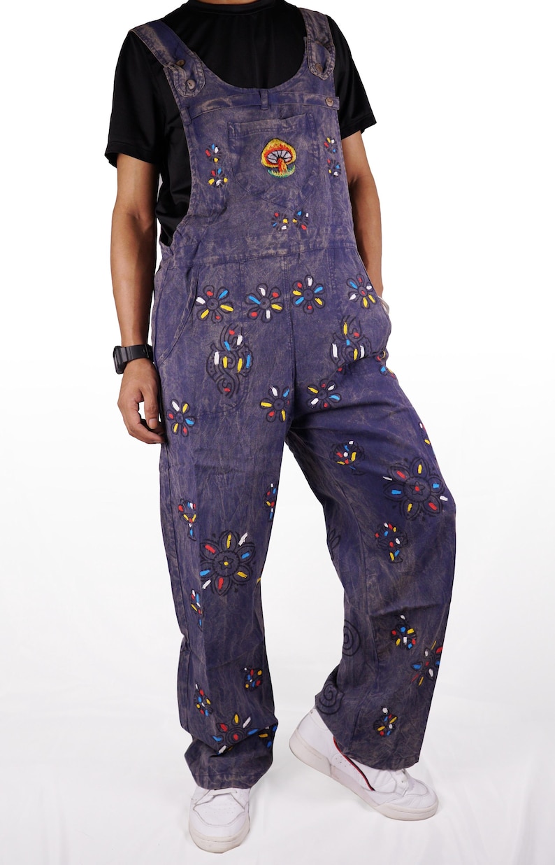 May include: Blue denim overalls with colorful floral embroidery and a mushroom design. The overalls have a relaxed fit and are perfect for a casual, bohemian look.
