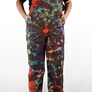 May include: A pair of tie-dye overalls with a brown background and colorful swirls of red, blue, green, and yellow. The overalls have a large circular design on the chest.