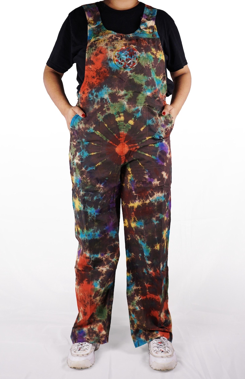 May include: A pair of tie-dye overalls with a brown background and colorful swirls of red, blue, green, and yellow. The overalls have a large circular design on the chest.