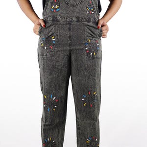 May include: Black denim overalls with colorful embroidered flowers and a mushroom design. The overalls have a relaxed fit and wide legs.