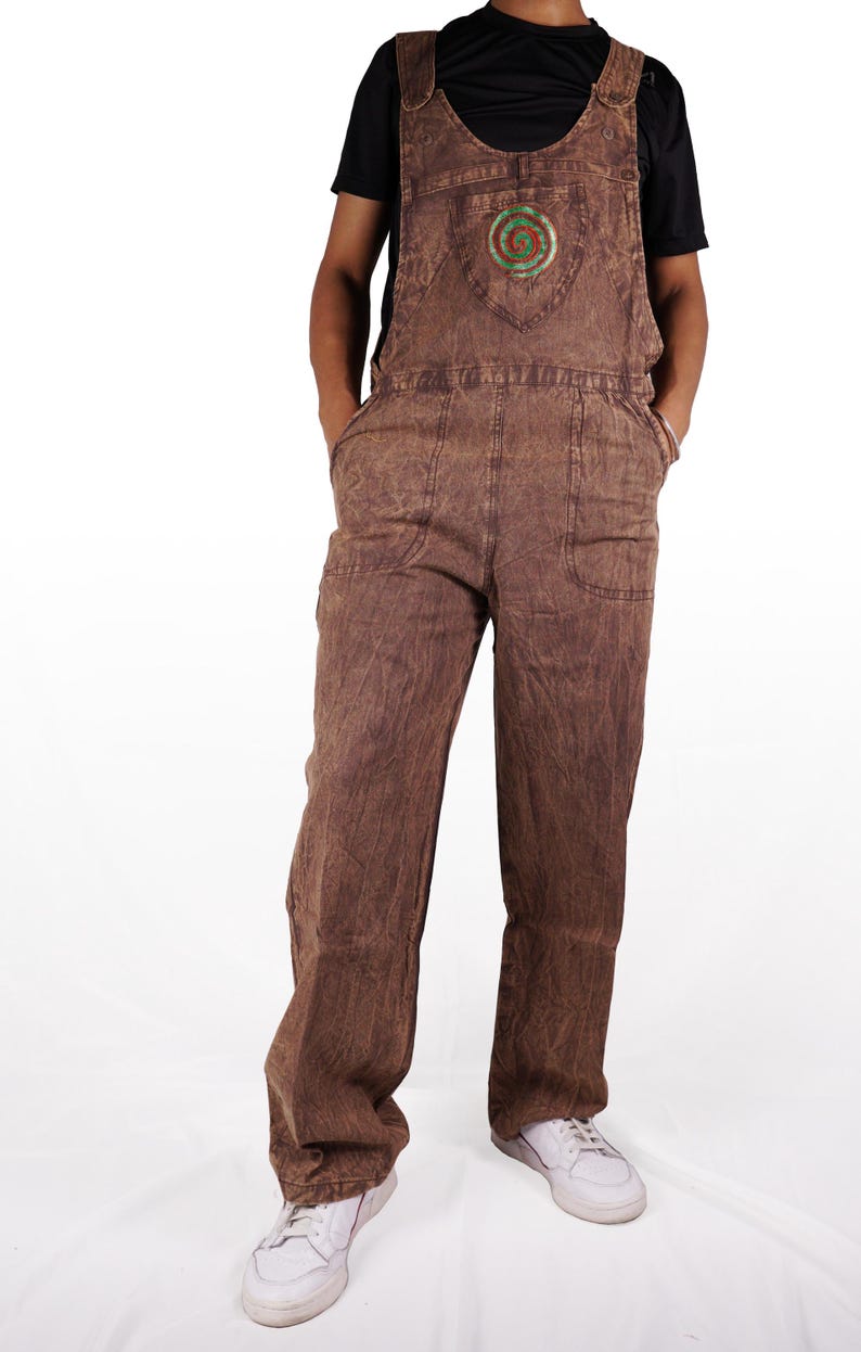 May include: Brown denim overalls with a green and red spiral design on the chest pocket. The overalls have adjustable straps and two front pockets.