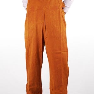 May include: A pair of orange overalls with a red and white circular design on the front pocket. The overalls have a relaxed fit and are made of a soft, comfortable fabric.