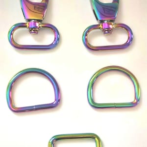 May include: A collection of iridescent metal hardware components. The image shows two swivel clasps, two D-rings, and a rectangular buckle with a bar. The hardware has a rainbow finish, with colors shifting from purple to green and gold.