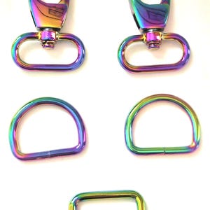 May include: A collection of iridescent metal hardware pieces, including two swivel clasps, two D-rings, and a rectangular slider buckle. The hardware has a rainbow finish, with colors shifting from purple to green and gold.
