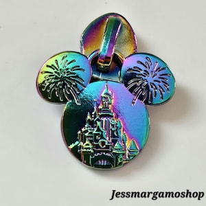May include: Iridescent zip pull with a Mickey Mouse design. The pull features a castle in the centre and fireworks on the ears. The text "Jessmargamoshop" is at the bottom.