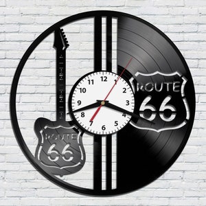 May include: Black vinyl record clock with a white clock face and black hands. The clock is decorated with a black silhouette of an electric guitar and a Route 66 sign.