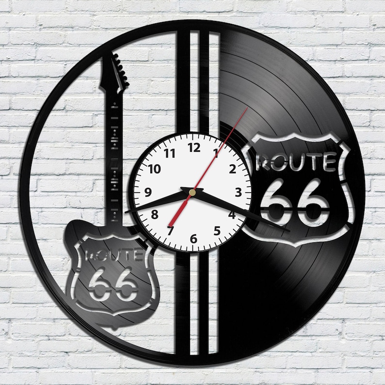 May include: Black vinyl record clock with a white clock face and black hands. The clock is decorated with a black silhouette of an electric guitar and a Route 66 sign.