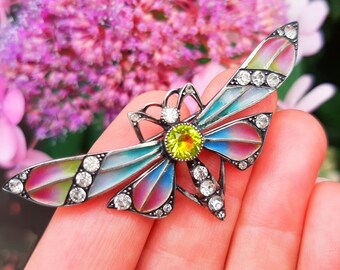 May include: A silver butterfly brooch with colorful enamel wings and clear rhinestones. The butterfly has a yellow center stone.
