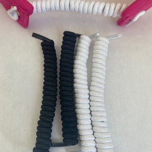May include: An assortment of coiled shoelaces in black and white, with a pink fabric piece attached to a white coiled lace. The laces are tightly wound and have plastic tips. The image is taken from a top-down perspective.