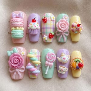 May include: A set of ten artificial nails with various 3D dessert designs. Each nail features a different design, including macarons, cupcakes, strawberries, roses, and lollipops. The nails are painted in pastel colors like pink, purple, and yellow, with a glossy finish.