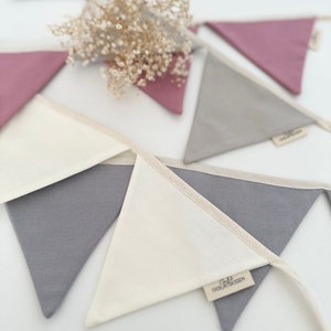 May include: A white and gray fabric bunting with a white triangle flag that says "Liebe Geburtsgeschenke". The bunting is strung together with a white string.