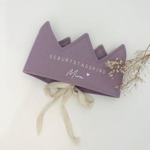 Könnte beinhalten: Eine lilafarbene Filzkrone mit einem weißen Band und dem Text "Geburtstagskind Mira" in weiß.