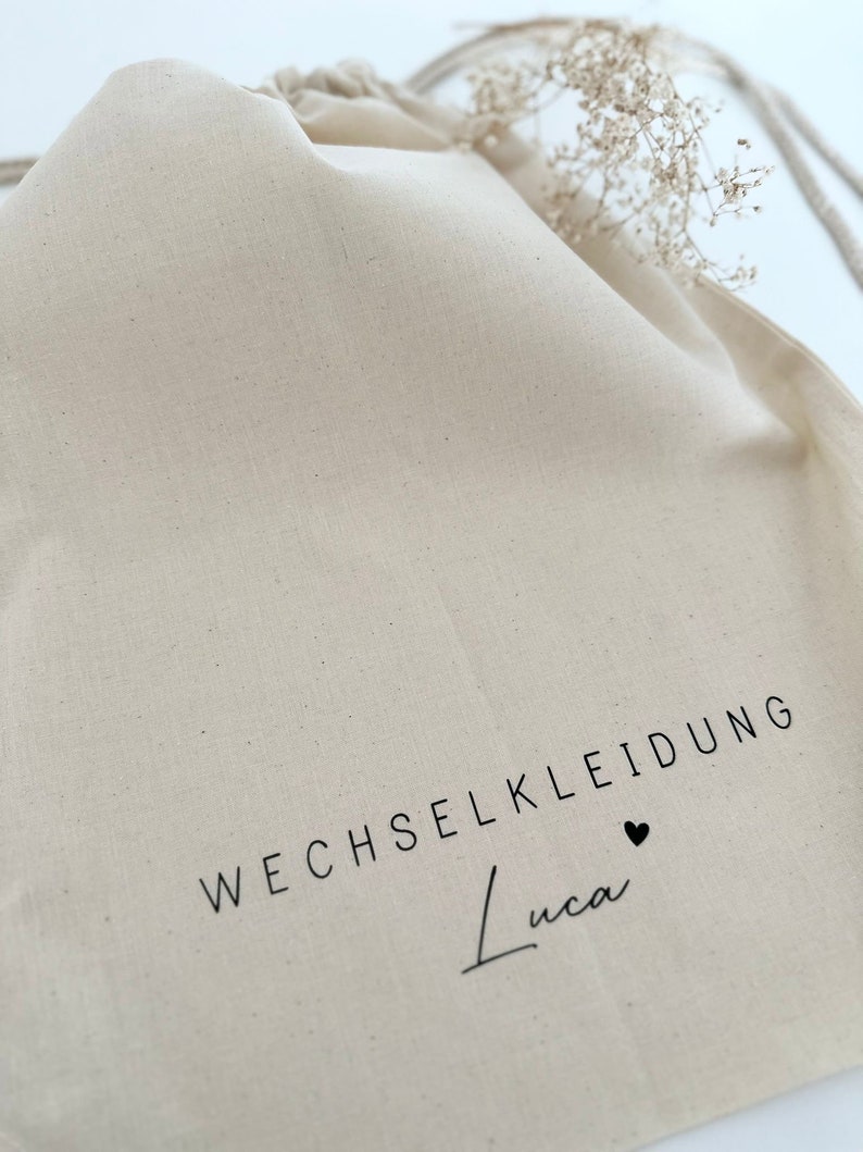 May include: A white drawstring bag with the text "WECHSELKLEIDUNG Luca" and a small black heart.