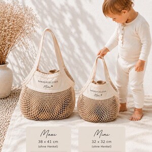 Puede incluir: Dos bolsas de lona beige y malla con dos asas cada una. Las bolsas presentan el texto "SANDSPIELZEUG Mika" con un icono de coraz&oacute;n. La bolsa grande mide 38 x 41 cm y la peque&ntilde;a mide 32 x 32 cm, sin incluir las asas.
