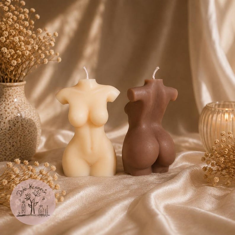 May include: Two torso-shaped candles, one cream and one brown, each featuring a single wick at the top. The cream candle displays the front of a human torso, while the brown candle displays the back. A circular logo with the text Deko-Kennerin is visible.