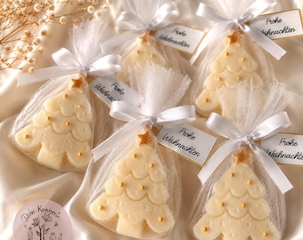 May include: Five cream-colored Christmas tree-shaped soaps packaged in white tulle bags with white satin ribbons and tags reading Frohe Weihnachten. Each soap features a gold star topper and small gold bead accents on the tree branches.