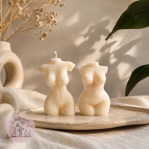 May include: Two off-white wax candles shaped like human torsos, each featuring a single centered wick at the top. The candles are sculpted with defined curves, including breasts, a narrow waist, and hips, presented in a smooth, matte finish.