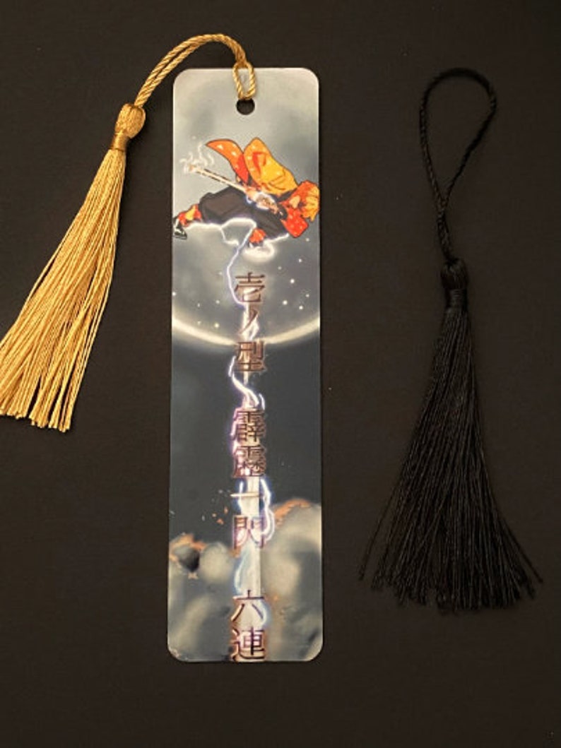 May include: A metal bookmark featuring an anime character with a sword, surrounded by lightning and a moon. The bookmark has a gold tassel and the text "鬼滅の刃" in Japanese.