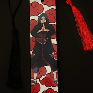 May include: A red and white bookmark with a black and red anime character on it. The bookmark has a red tassel.