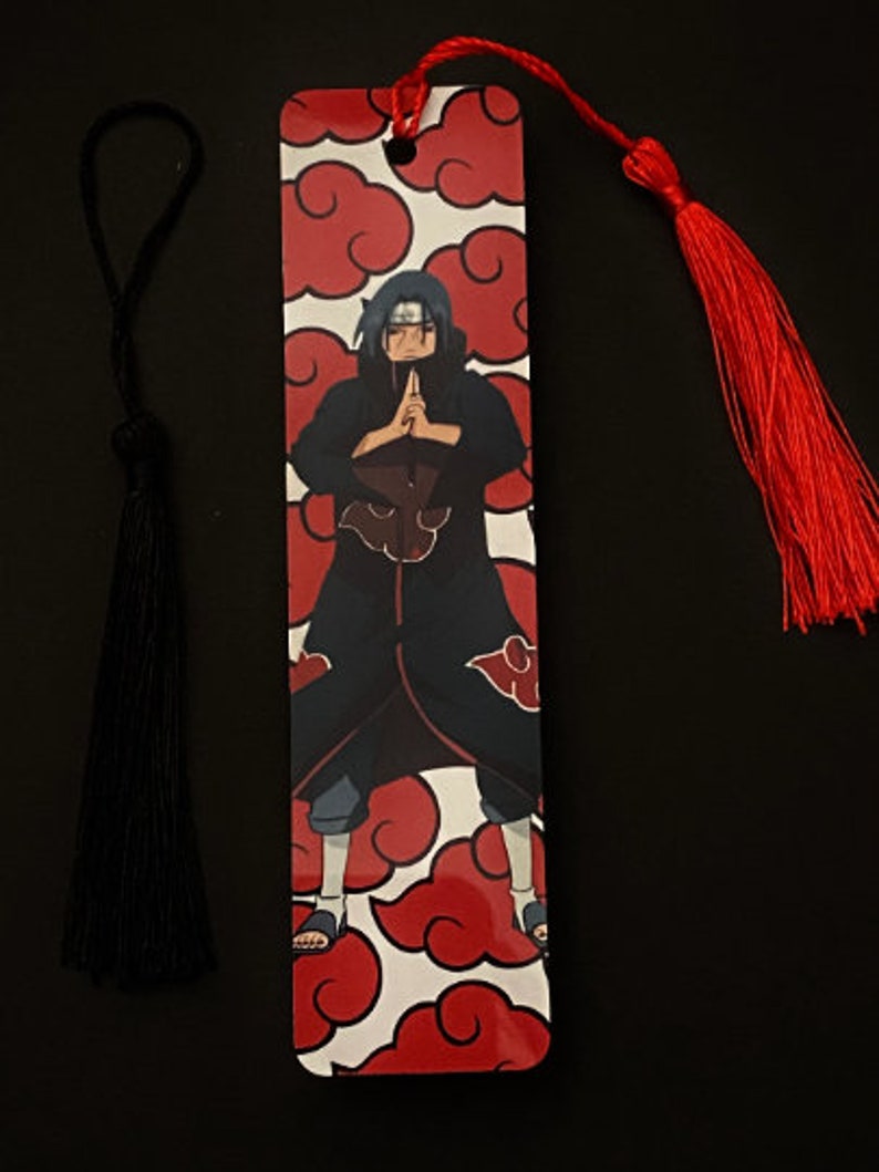 May include: A red and white bookmark with a black and red anime character on it. The bookmark has a red tassel.