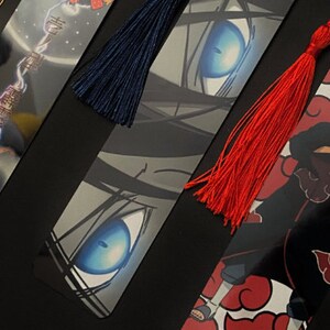 May include: Three different anime bookmarks with colorful tassels. The first bookmark features a character with a red and yellow outfit. The second bookmark features a close-up of a character's eye with a blue iris. The third bookmark features a character with red clouds and a black and red outfit.
