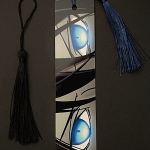 May include: A black and white bookmark with a close-up of a blue eye. The bookmark has a black tassel and a blue tassel.