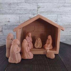 May include: A terracotta nativity scene featuring a stable and several figures. The figures include Mary, Joseph, baby Jesus, and other biblical characters. The set is made of a reddish-brown clay material.